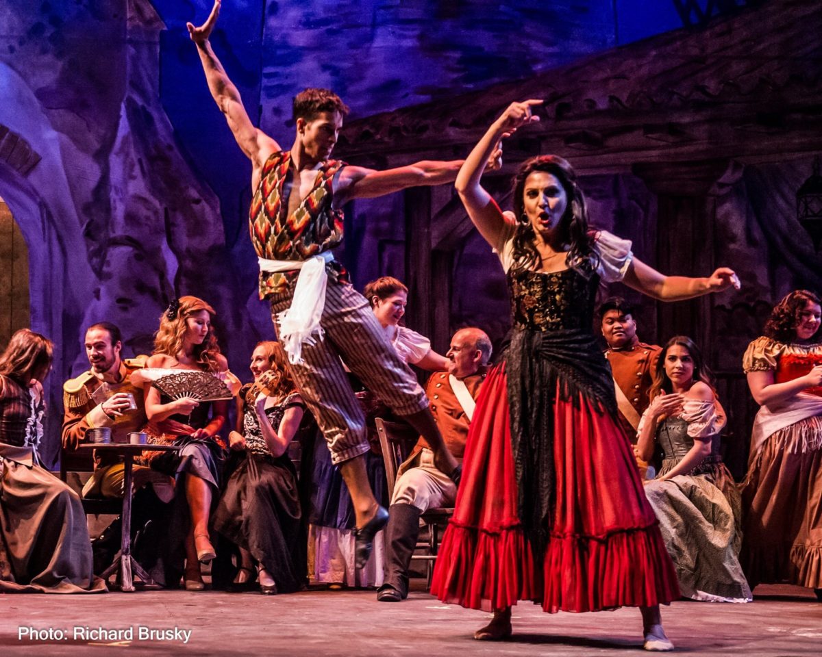 Carmen poses as a male dancer jumps high behind her.