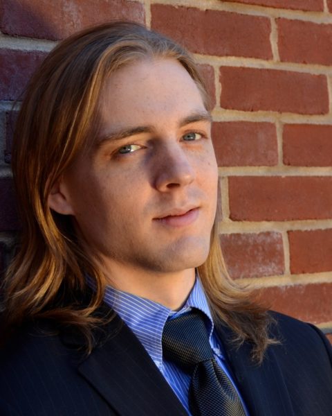 Rob McGinness, Baritone, smiling in formal wear in front of a brick wall.