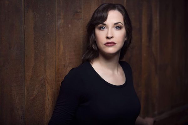 Shannon Jennings, Soprano, in a black outfit against a wood paneled wall.