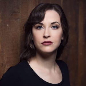 Shannon Jennings, Soprano, in a black outfit against a wood paneled wall.