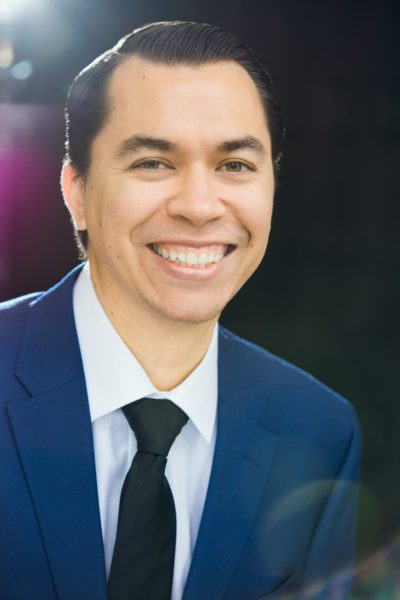 Norman Espinoza, Bass, smiling in a suit and tie.