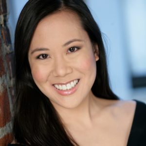 Katie Leung, pianist, smiling in black formal clothing against a light background.