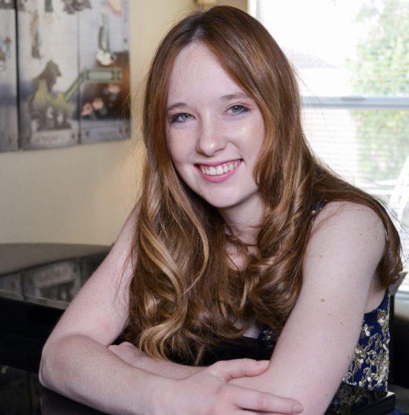 Emily Clements, a young red-headed woman smiling while resting on her elbows and leaning forward.