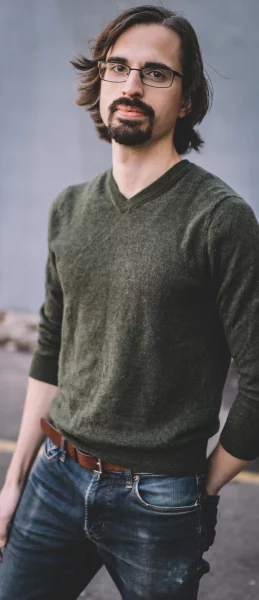 Evan L. Snyder, standing casually in a dark green cashmere sweater and jeans. He has long dark hair, glasses, and facial hair.