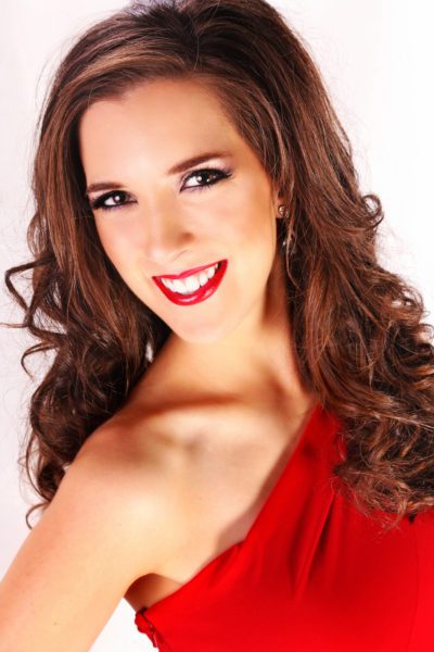 Genevieve Fulks, formally dressed in a red gown, smiling in studio lighting.