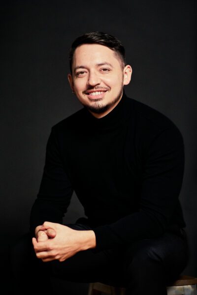 Manuel Arellano, a Hispanic man with light facial hair in a black turtleneck, studio photo against a dark background.
