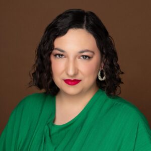 Claudia Affan, a light-skinned woman with shoulder-length dark hair and formal makeup in a professional studio photo. She wears a bright green loose-fitting blouse.