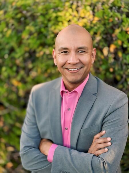 Octavio Moreno stands with arms crossed in an outdoor setting, wearing a smart suit and shirt.