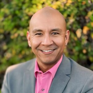 Octavio Moreno stands with arms crossed in an outdoor setting, wearing a smart suit and shirt.