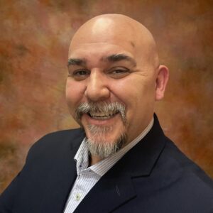 Adelmo Guidarelli, a bald man with a greying goatee, smiles and poses with arms crossed in a formal suit.