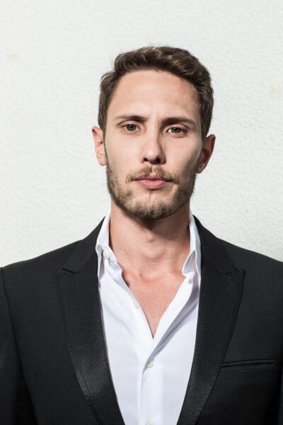 Colin Ramsey, a Chinese-American man with light facial hair, poses in a dark suit and a neutral serious expression.