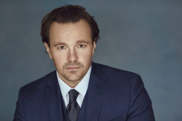 Daniel Scofield dressed in a suit and tie with a neutral expression and studio lighting.