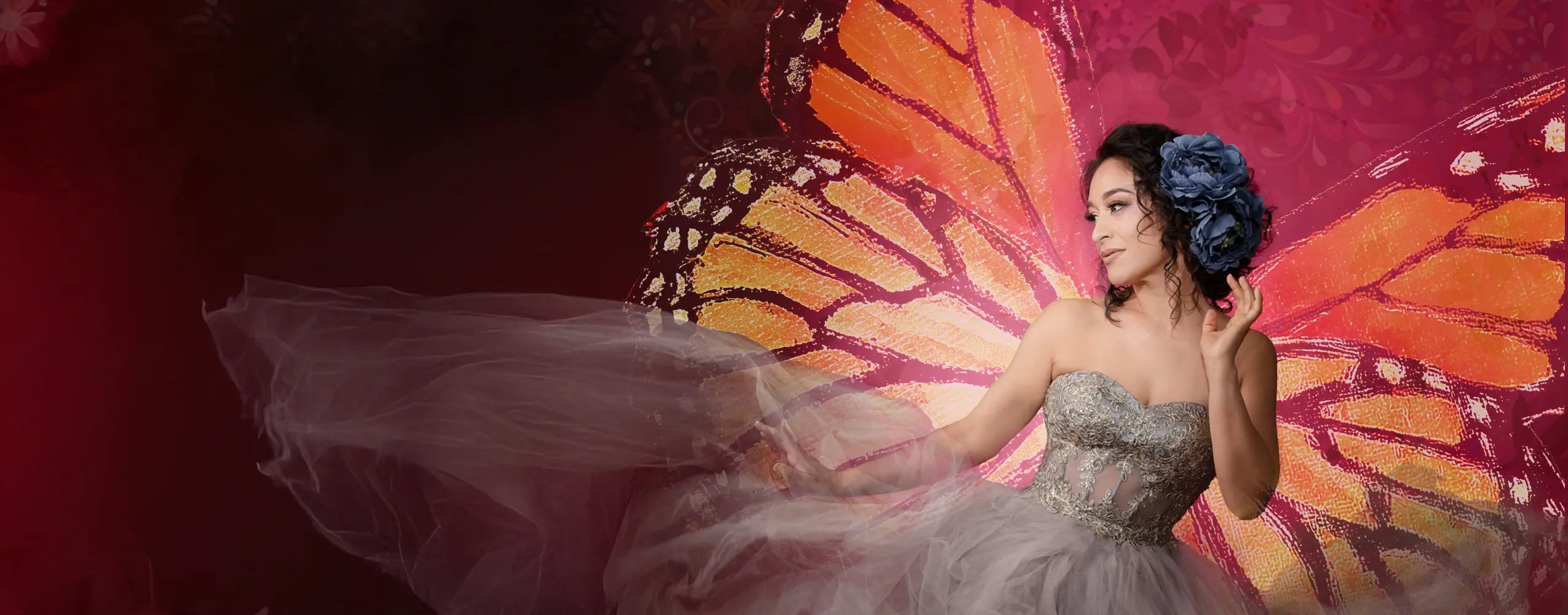 Cecilia Violetta Lopez poses in a dance-like stance wearing a floor-length gown. Behind her, two ethereal butterfly wings glow over a flowery background.