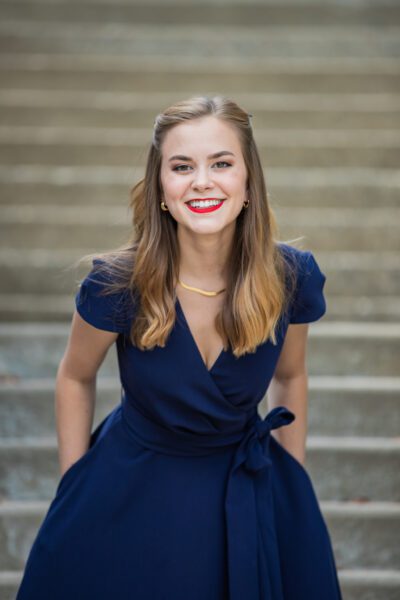 Tori Tedeschi Adams, a young caucasian woman smiles facing the camera in a semi-formal A-line dress.