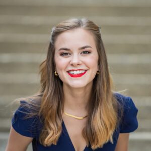 Tori Tedeschi Adams, a young caucasian woman smiles facing the camera in a semi-formal A-line dress.