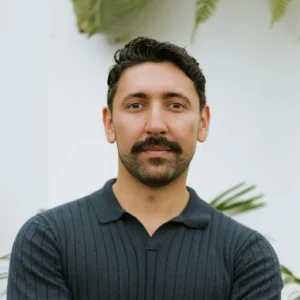 Efrain Solis stands with arms crossed, outdoors amid verdant greenery in casual attire.
