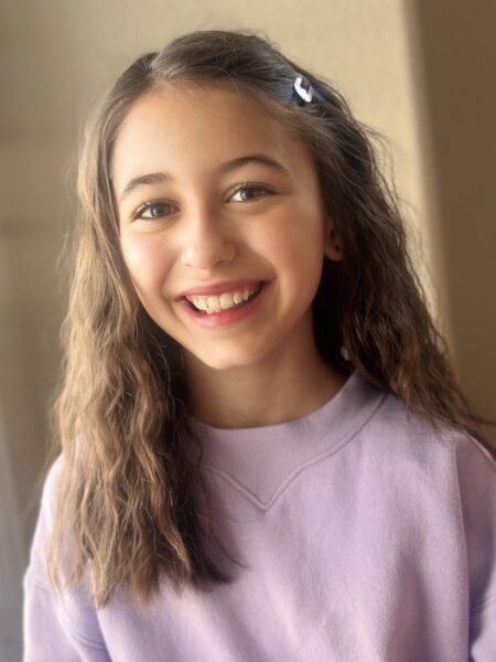 Josephine Valentina Monastero, a young girl smiling in casual attire and warm lighting.
