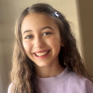 Josephine Valentina Monastero, a young girl smiling in casual attire and warm lighting.