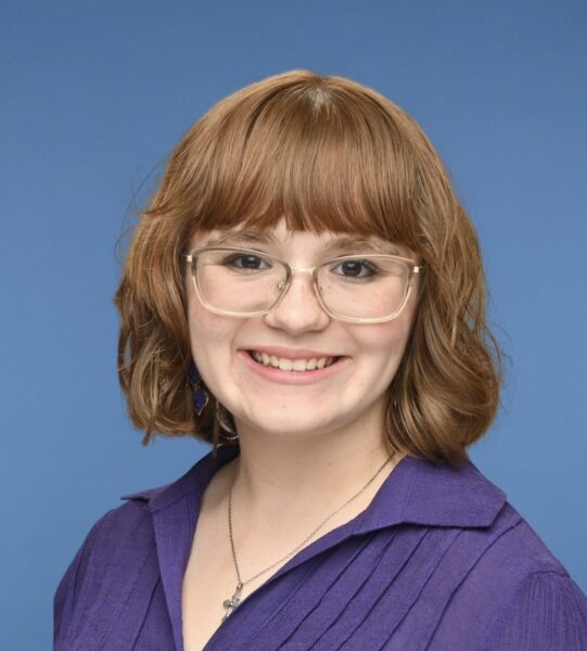 Sylvia Holladay Lenker smiles in casual attire against a studio backdrop.