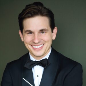 Christopher James Ray, a short-haired Caucasian man dressed in a formal tuxedo, holding a conductor's baton.
