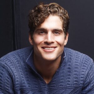Keith Milkie, smiling in studio lighting. He wears a dark sweater.