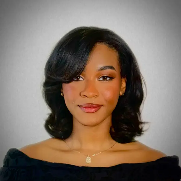 Alexia Hamilton, a young black woman dressed in a dark blouse smiling against a grey studio wall.