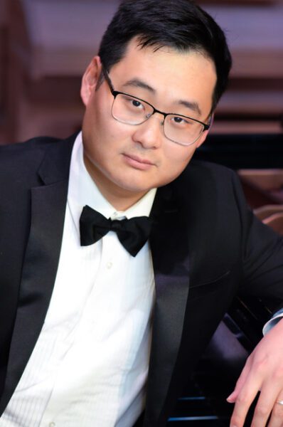 Jae Ahn-Benton poses in a tuxedo with his piano.