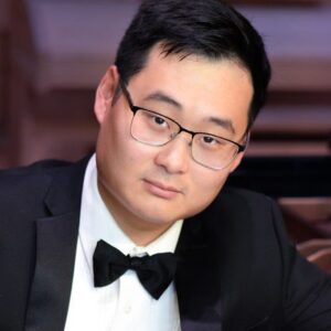 Jae Ahn-Benton poses in a tuxedo with his piano.