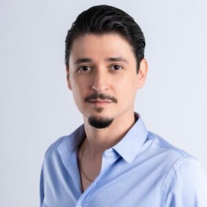 Isaac Herrera, a slim young Mexican man with short hair, a mustache, and a goatee, smiles gently while wearing a button-down collared shirt.