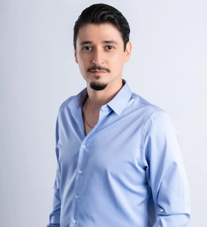 Isaac Herrera, a slim young Mexican man with short hair, a mustache, and a goatee, smiles gently while wearing a button-down collared shirt.