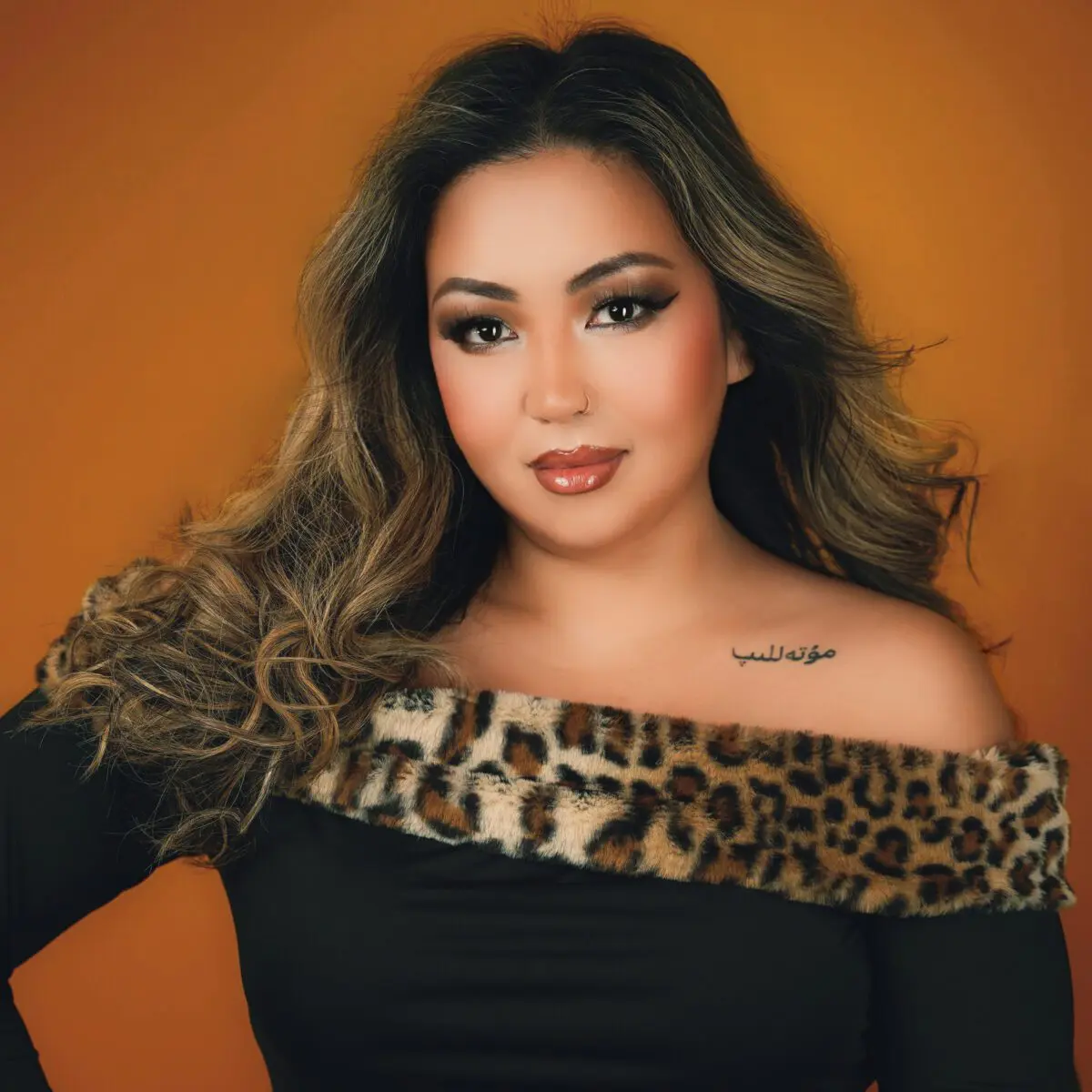 Soprano Nina Mutalifu, a tan-skinned woman with long dark hair, smiles pleasantly while wearing a dark, formal top lined with faux leopard fur.