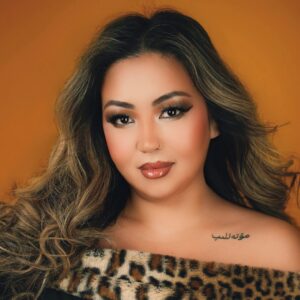 Soprano Nina Mutalifu, a tan-skinned woman with long dark hair, smiles pleasantly while wearing a dark, formal top lined with faux leopard fur.
